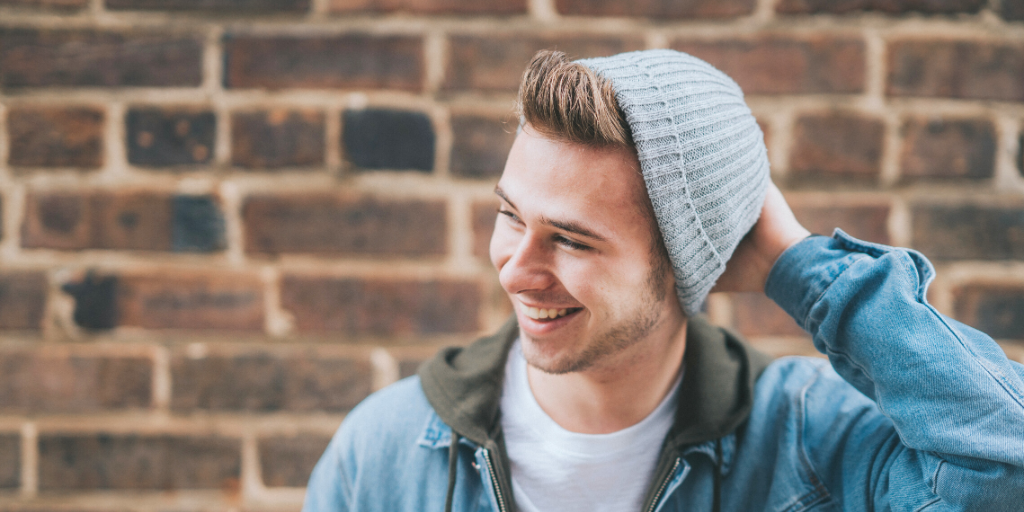 A your man holding a hand on his hat (on his head) while smiling away from the camera