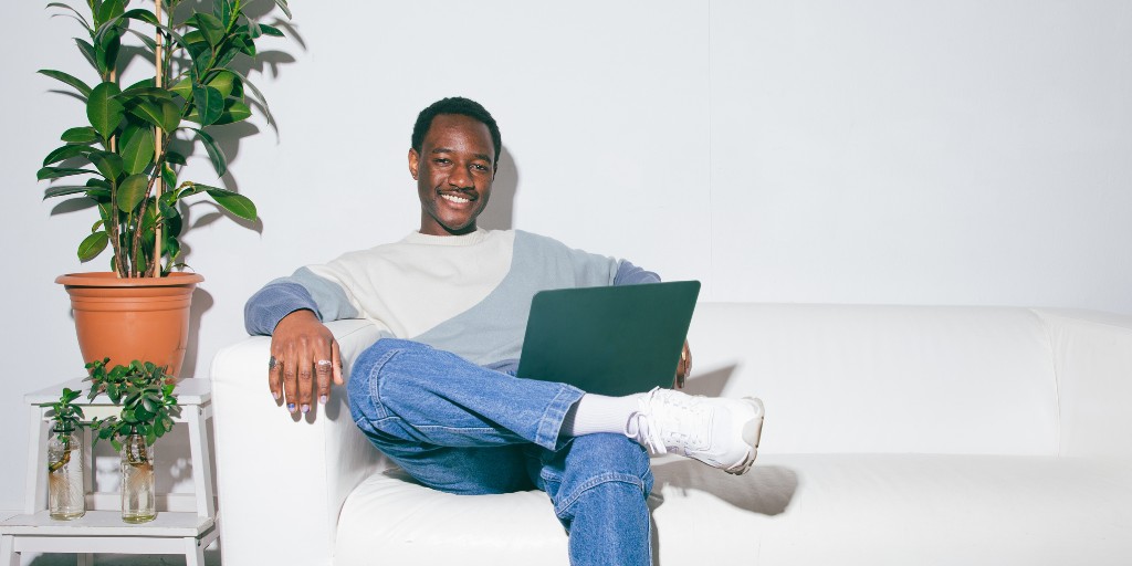 Man sitting on sofa with laptop on folded knee and smiling at camera