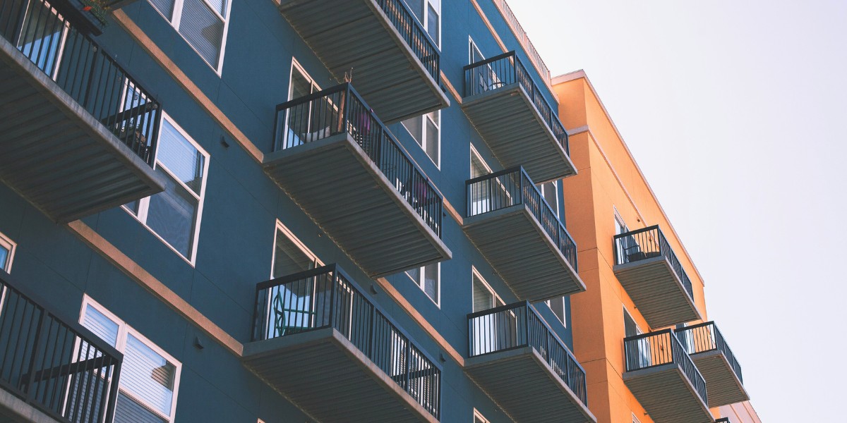 Low-angle view of an apartment block with rows of balconies on teal and orange cladding