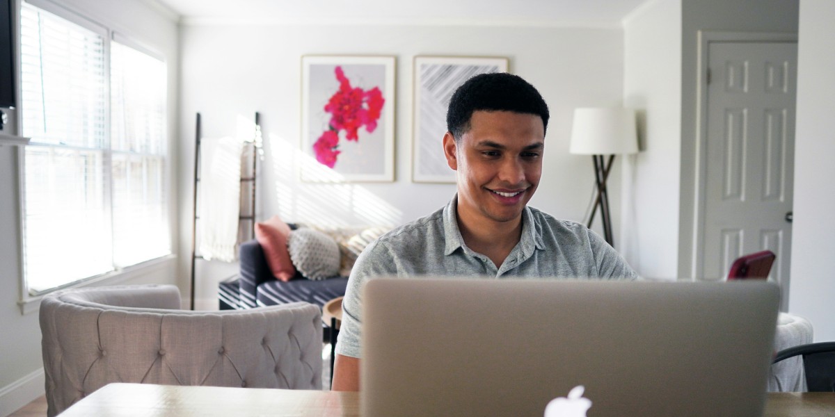A man works at a laptop at a dining table in a bright living room
