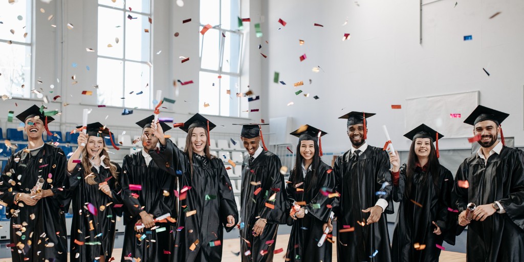 Group of graduating students in graduation robes. There is confetti in the air and everyone is smiling.