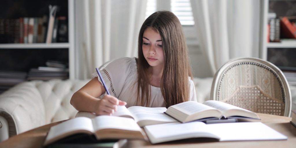 Young female student writing notes. There are open books on the table.