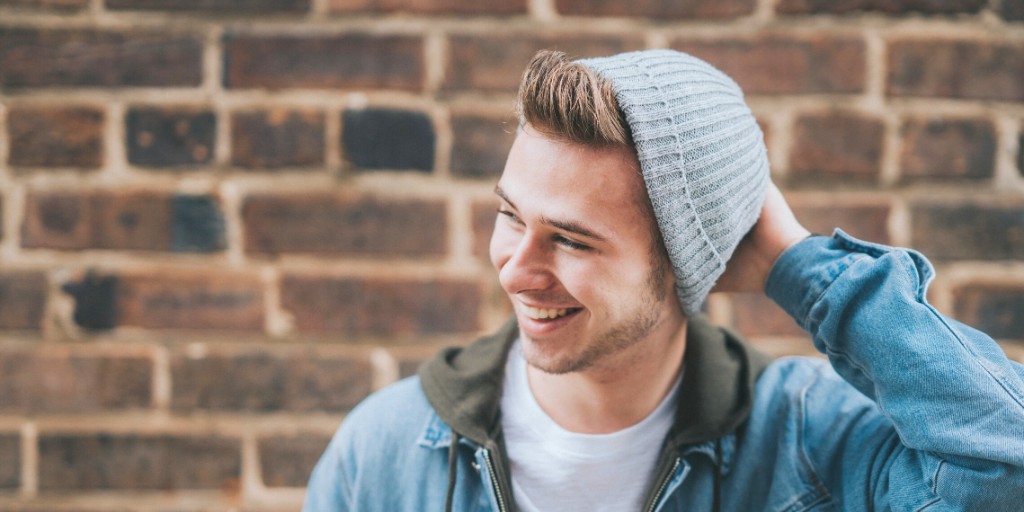 A your man holding a hand on his hat (on his head) while smiling away from the camera