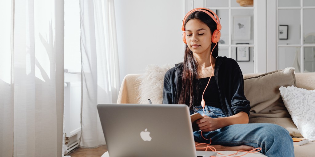Female student working at laptop, while wearing headphones.