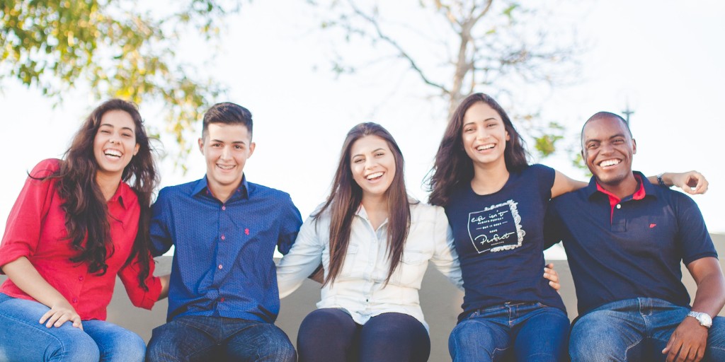 Smiling students sitting on a wall, linking arms and smiling at the camera